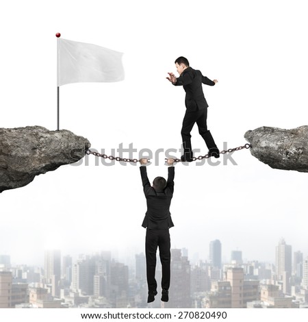 Businessman balancing on the cracking rusty iron chains another man holding connect two cliffs and walking toward white flag with urban scene skyline background, business teamwork concept.