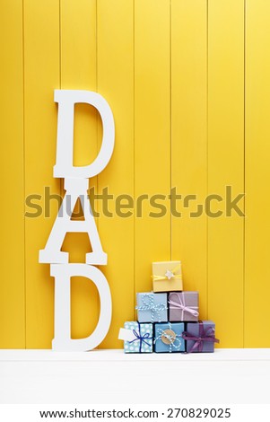 DAD text letters with little gift boxes on yellow wooden background