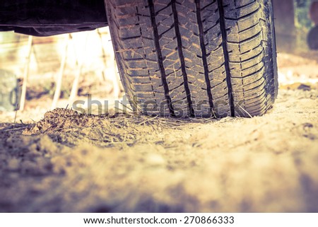 Closeup car tire on the ground. Wheel tracks on dirt, shallow depth of field (DOF) tyre in focus. Vintage picture style