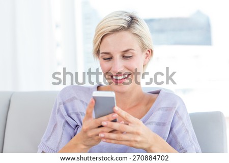 Pretty blonde woman texting with her mobile phone in the living room
