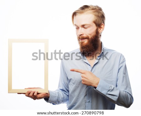 Copy space in picture frame. Handsome young bearded man in blue shirt holding a picture frame and pointing it with smile while standing isolated on white background 