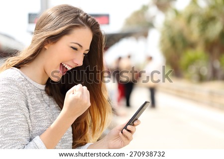 Euphoric woman watching her smart phone in a train station while is waiting  Royalty-Free Stock Photo #270938732