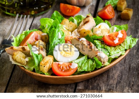 Caesar salad with croutons, quail eggs, cherry tomatoes and grilled chicken in wooden plate on dark rustic table Royalty-Free Stock Photo #271030664