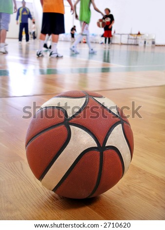 Basketball in wooden floor with players practicing in the background.