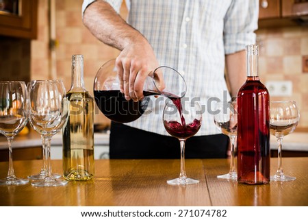 A man pours red wine from the decanter into a glass, home kitchen interior