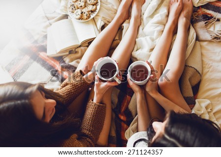 Soft photo of two  sisters  on the bed with old books and cup of tea in hands wearing cozy sweater , top view point. Two best friends enjoying morning. Royalty-Free Stock Photo #271124357