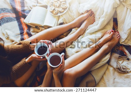 Soft photo of two  sisters  on the bed with old books and cup of tea in hands wearing cozy sweater , top view point. Two best friends enjoying morning. Royalty-Free Stock Photo #271124447