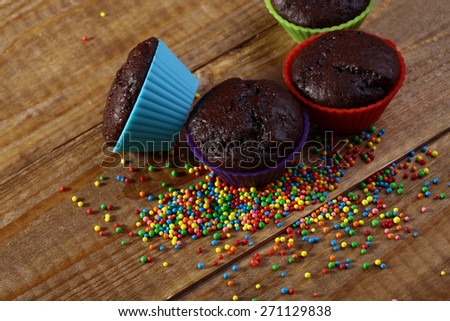 Chocolate cup cakes and colored small sweets on wooden table top, horizontal picture