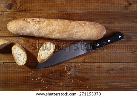Sliced up baguette and sharp metalic knife on wooden table top, horizontal picture