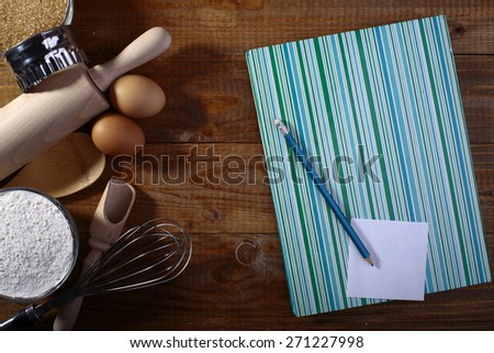 Collection of ingredients and appliances for making pastry with recipe book on wooden table top, horizontal picture
