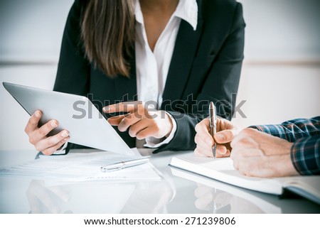 Two business people in a meeting discussing information on a tablet-pc and taking notes as they work together as a team, close up view of their hands seated at a desk Royalty-Free Stock Photo #271239806