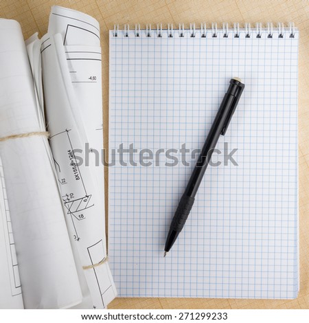 Architectural blueprint and blueprint rolls near checkered blank paper with pen on graph paper background. Copy space