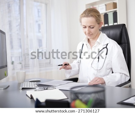 Adult Female Clinician Sitting at her Desk and Reading Back her Written Medical Reports Seriously.