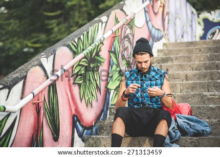 young handsome bearded hipster man using smartphone and listening music with earphones in the city