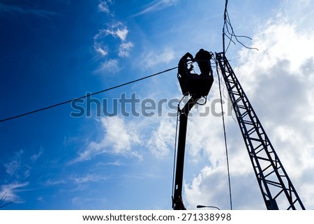 Technician's works in a bucket high up on a power pole. Traffic warning sign.