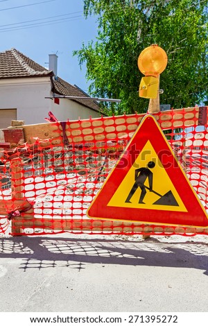 Construction site is protected by several traffic signs and orange fence with flashing beacon lights for safety.