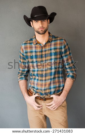 Brave cowboy. Handsome young man wearing cowboy hat and looking at camera while standing against grey background  Royalty-Free Stock Photo #271431083