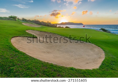 Sand bunkers and a red flag at the beautiful golf course at the ocean side at sunset, sunrise time.