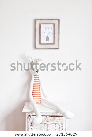 Striped bunny sitting on the bedside table and picture frame on the white wall
