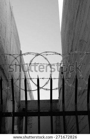 An inner city fence with sharpened vertical bars, barbed wire and concertina wire conveys the message. "Keep Out." (monochrome image)