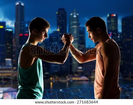 sport, competition, strength and people concept - two young men arm wrestling over night city background