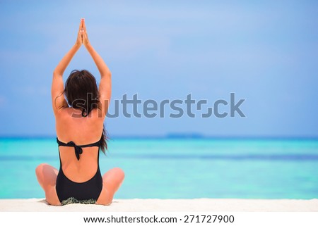 Healthy young woman sitting in yoga position meditating on the beach