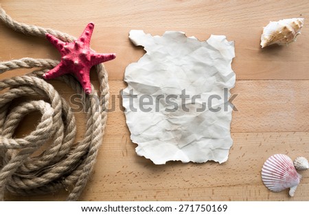 Old blank piece of paper lying on wooden boards with ropes and seashells