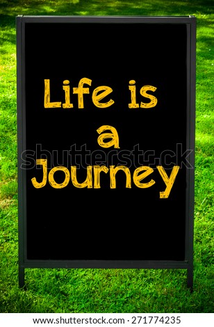 LIFE IS A JOURNEY  message on sidewalk blackboard sign against green grass background. Copy Space available. Concept image