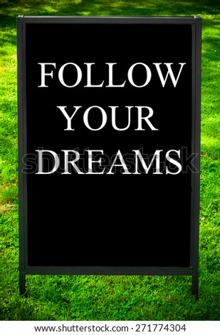 FOLLOW YOUR DREAMS  message on sidewalk blackboard sign against green grass background. Copy Space available. Concept image