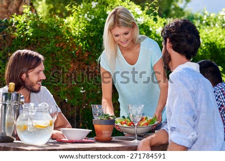 young woman serving salad to friends gathering at outdoor garden party Royalty-Free Stock Photo #271784591