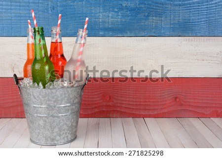 A bucket of soda bottles with drinking straws against a red, white and blue background for a 4th of July picnic, with copy space.