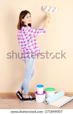 Beautiful woman paints wall in room