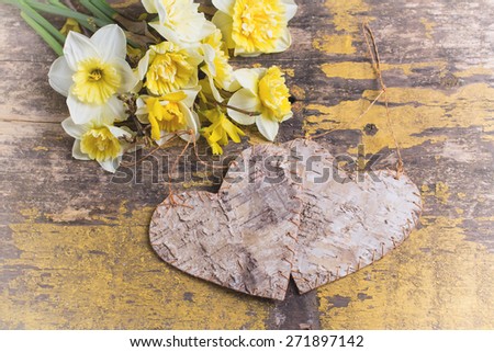 Fresh  spring yellow narcissus  flowers and two decorative heart on yellow weathered wooden background. Selective focus. Place for text. Toned image. 