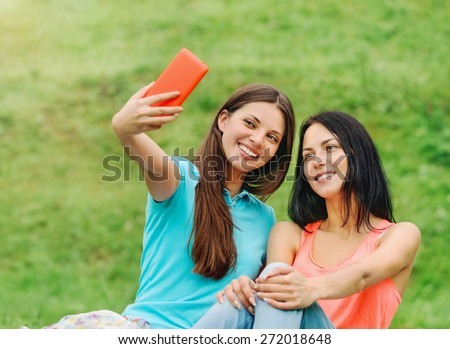 two happy women friends laughing and sharing social media pictures in a smart phone on picnic at the park, lifestyle concept