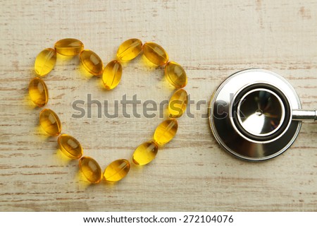 Heart of cod liver oil and stethoscope, on wooden background