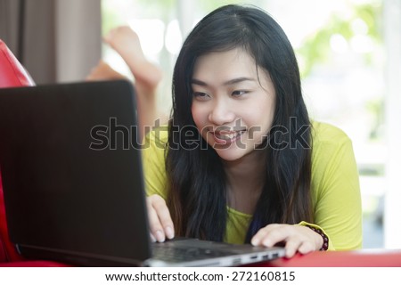 Asian woman lying on sofa with notebook  in living room