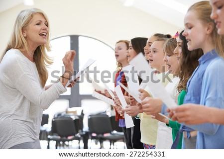 Children In Singing Group Being Encouraged By Teacher Royalty-Free Stock Photo #272254331
