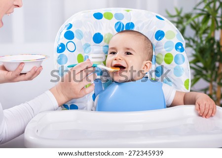 Smiling baby boy enjoy at feeding time in kitchen