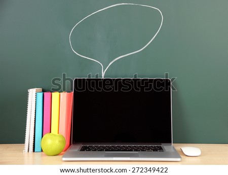 Laptop on table, on green blackboard background