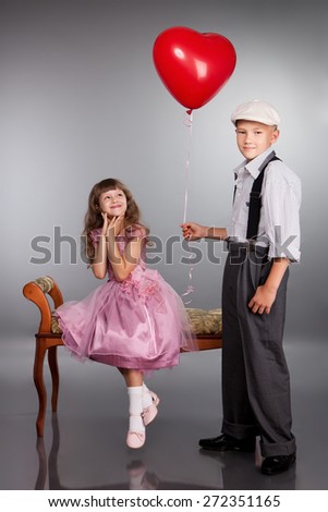 The boy gives a red balloon to the girl. Photo in retro style.