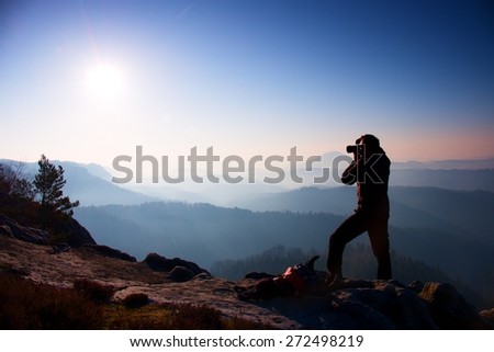 Professional photographer takes photos with mirror camera on peak of rock. Dreamy fogy landscape, spring orange pink misty sunrise in beautiful valley below. Professional photographer.Dreamy landscape