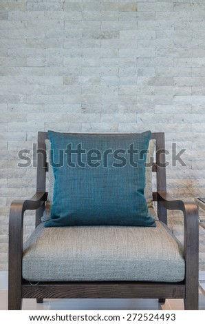 wooden chair with blue pillow in living room with rock wall as background