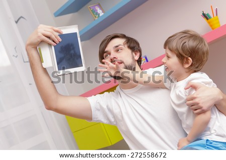 No cartoons. Young father taking away a tablet device from his small son who stretches out his hand to grab it 