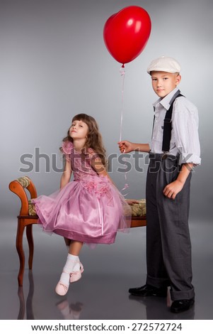 The boy gives a red balloon to the girl. Photo in retro style.