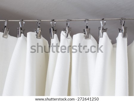 cream-colored curtain hanging on a string on a metal hook in white ceiling illuminated by daylight Royalty-Free Stock Photo #272641250