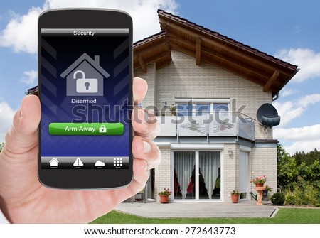 Close-up Of Person Hand Holding Mobile Phone With Home Security System