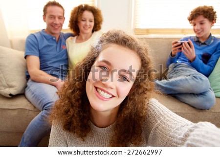 Portrait of a happy young girl taking selfie with parents in the background 