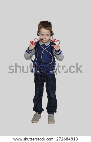 Serious little boy in headphones tangled in wires compares two identical cables on gray background - Technology and communication concept
