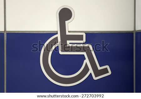 Grey wheelchair sign on the white and blue wall. Public restroom signs with a disabled access symbol.