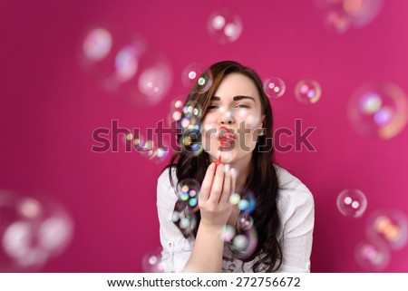 Playful woman blowing party bubbles at the camera as she celebrates a special occasion or birthday, over magenta Royalty-Free Stock Photo #272756672